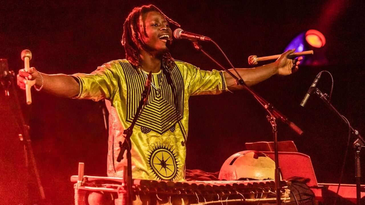 N'famady Kouyaté singing live, arms raised, with balafon