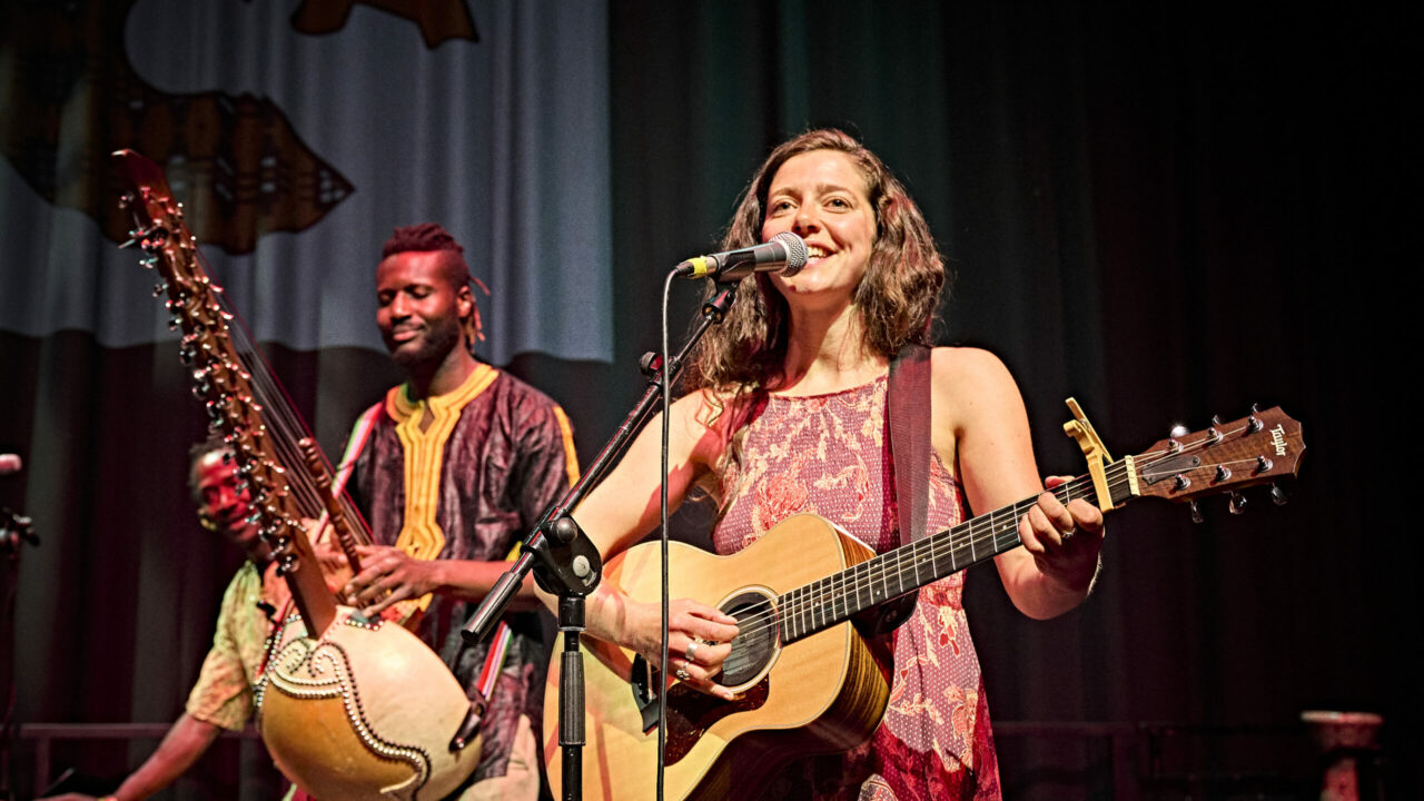 Image of Eve goodman holding a guitar and suntou susso holding a kora on stage